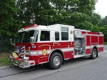 Front left exterior view of a red pumper with chrome bumper, side pump panel, and rear compartments.