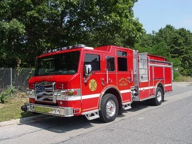 Front left exterior view of a red pumper with chrome bumper, grille, and side body compartments.