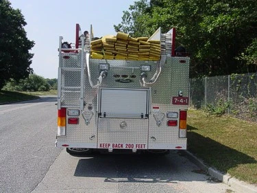 Straight rear view showing hosebed load, rear roll-up door, warning lights, and tailboard.