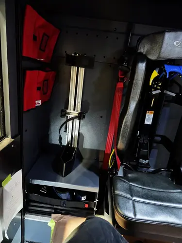 Interior crew-seat area view showing seat mount, red restraint, and storage shelf