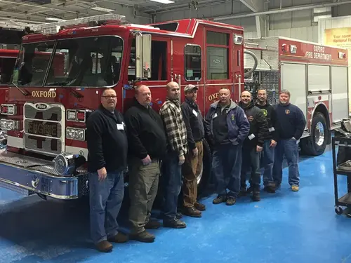 Front-left view of pumper inside apparatus bay with a line of firefighters in front