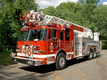 Aerial ladder truck front-left exterior view showing enclosed cab and ladder bed
