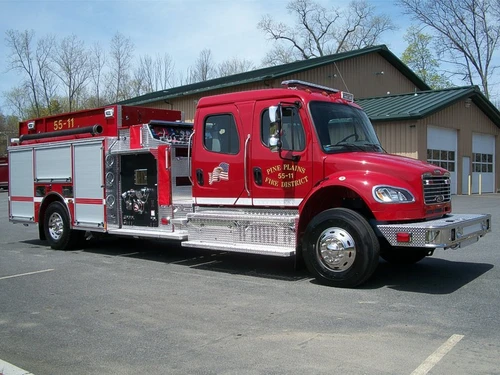 Front-right exterior view of a pumper with commercial cab, exposed pump panel, and side compartments.