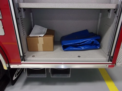 Open side compartment showing a cardboard box and folded tarp on shelf