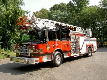 Front left exterior view of an aerial ladder truck with stowed ladder, front bumper, and side compartments.