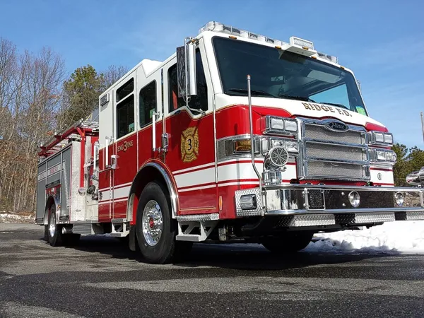 Low front right exterior view of a red-and-white pumper showing chrome bumper, cab, and side compartments.