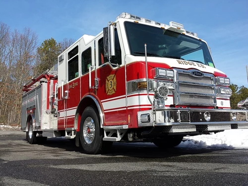 Low front right exterior view of a red-and-white pumper showing chrome bumper, cab, and side compartments.