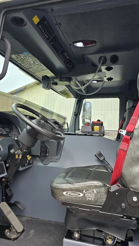 Driver cockpit view showing steering wheel, instrument cluster, and overhead switch panel