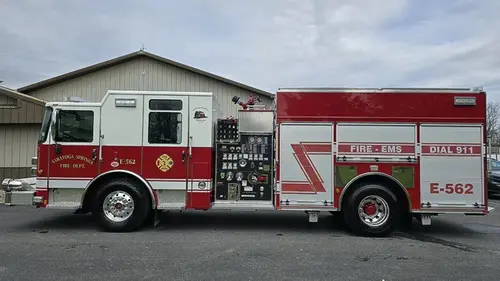 Pumper driver-side profile view showing pump panel, side compartments, and wheel area