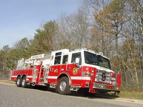 Low front-right wide view showing the aerial ladder body, tandem rear axles, and front outrigger post.