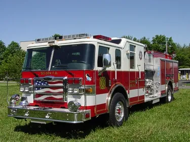 Front-right exterior view of a pumper with chrome bumper, enclosed cab, and side pump panel area.