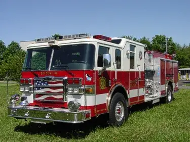 Front-right exterior view of a pumper with chrome bumper, enclosed cab, and side pump panel area.