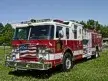 Wide front-right view of the pumper parked on grass with cab and side body visible.