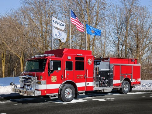 Front-left exterior view of a red pumper showing the cab, pump panel section, and side compartments.