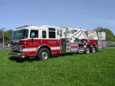 Front left exterior view of a mid-mount tower ladder with tandem rear axles and stowed aerial.