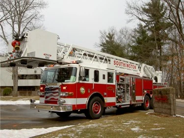 Front-left exterior view of a tower ladder with bucket, side compartments, and tandem rear axles.