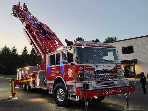 Tower ladder truck front-left exterior view with aerial ladder raised at dusk