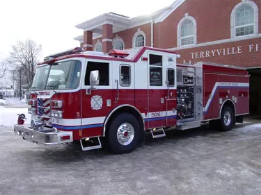 Pumper front-left exterior view parked near station showing cab and side compartments