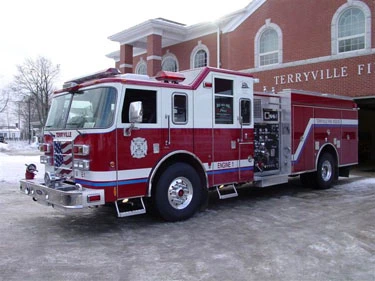 Pumper front-left exterior view parked near station showing cab and side compartments