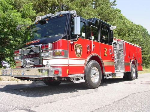 Front-left exterior view of a pumper showing the cab, side pump panel section, and rear body compartments.