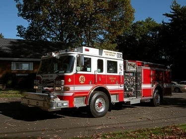 Front-left exterior view of a rescue pumper with chrome bumper, cab, and exposed pump panel section.