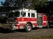 Wide front-left view of the rescue pumper parked near trees with full side body visible.