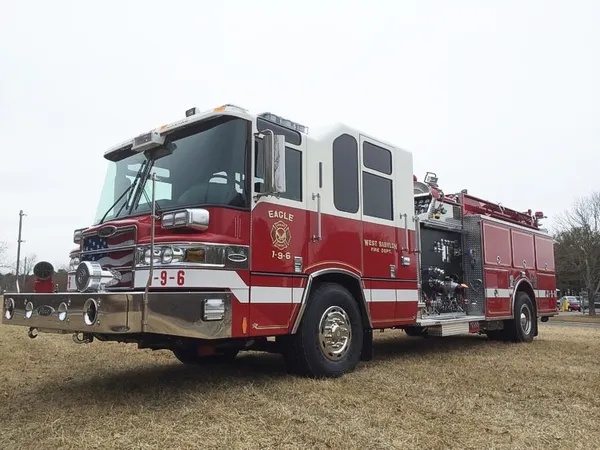 Front-left exterior view of a pumper showing the cab, bumper, pump panel section, and side compartments.