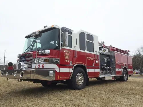 Front-left exterior view of a pumper showing the cab, bumper, pump panel section, and side compartments.