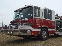 Wide front-left view of the pumper parked on grass with the cab and pump panel section visible.