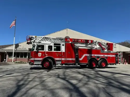 Driver-side profile showing tower ladder truck parked near station