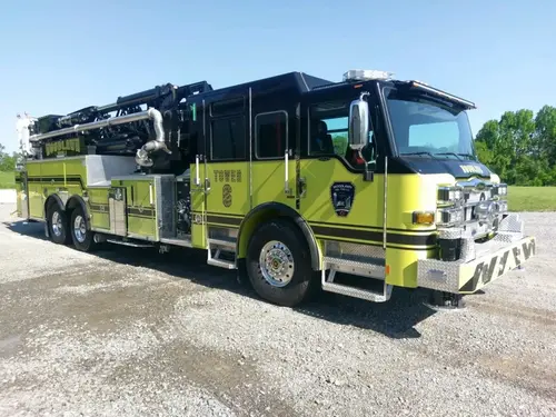 Tower ladder truck front-left exterior view showing enclosed cab and black ladder bed