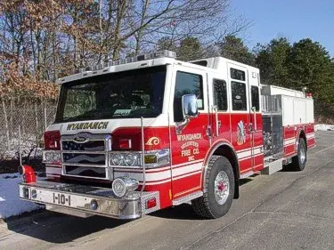 Front left exterior view of a red-and-white pumper with chrome bumper, cab lights, and side compartments.